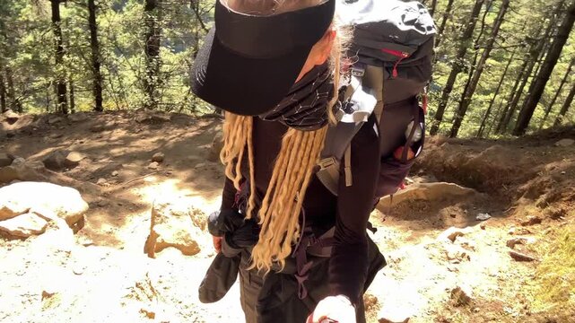 Female trekker with backpack and dreadlocks filming herself while hiking uphill on Everest Base Camp trail, Nepal. Tired but determined, high altitude trekking in  Himalayas