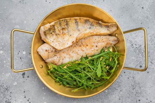 Pan fried pike perch fillet served with fresh greens in skillet, healthy freshwater white fish meal.