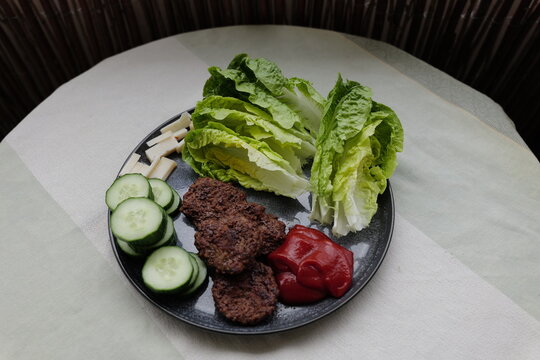 Gesundes Mittagessen: ein Teller mit Buletten, R&ouml;mersalat, Gurken und Ziegenk&auml;se, dazu ein  Klecks Ketchup.
