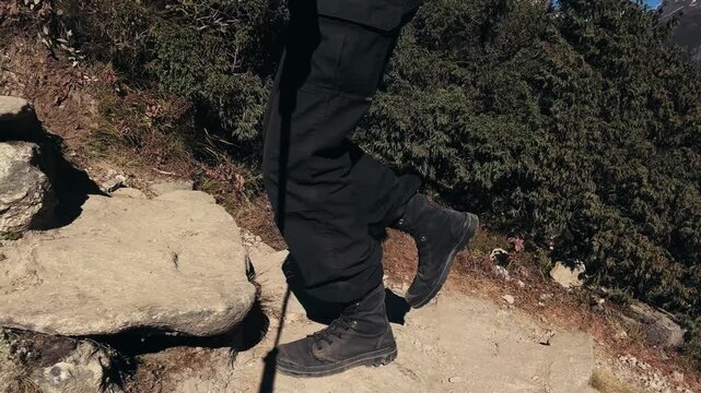 Close-up of trekking legs climbing slowly in Everest region, Nepal. Careful uphill movement at high altitude with dramatic Himalayan mountains, endurance and breathing control