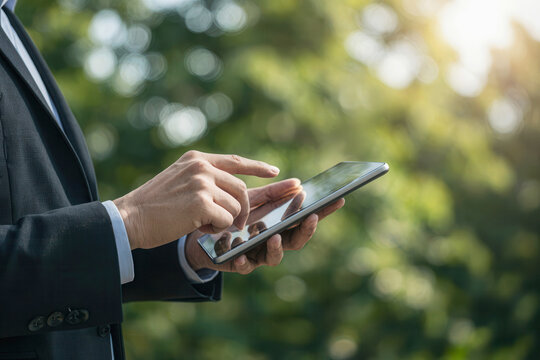 Businessman using tablet with eco green tree background, man hand holding tablet in sustainable technology
