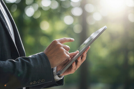 Businessman using tablet with eco green tree background, man hand holding tablet in sustainable technology