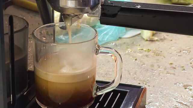 Espresso coffee dripping into clear glass cup from machine. Freshly brewed beverage preparing in kitchen. Caffeine breakfast drink with crema foam, drink concept.