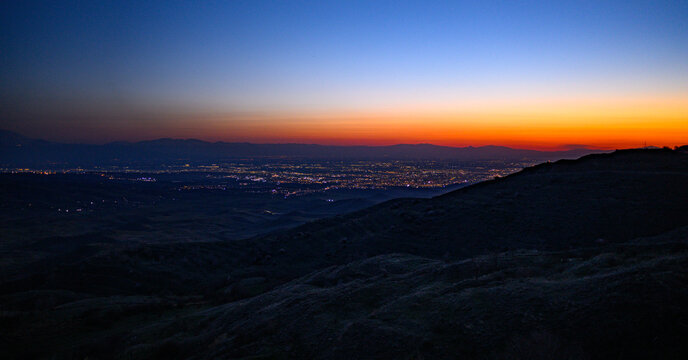 Nightfall over cityscape from elevated hillside with glowing lights