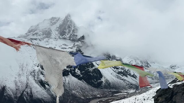 Tibetan prayer flags fluttering against cloudy snowy mountains in Everest region, Nepal. Dramatic Himalayan landscape with mist and moving clouds, atmospheric slow motion shot