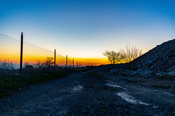 Fototapeta premium Sunset view with fence, dirt path, and rocky terrain