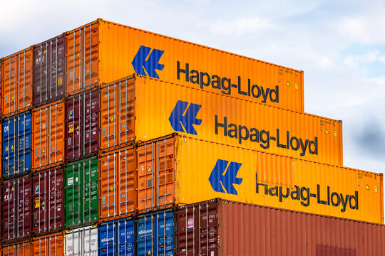 Symbolbild: Mehrere gestapelte orangefarbene Frachtcontainer der Hamburger Reederei Hapag-Lloyd, umgeben von weiteren bunten Containern verschiedener Reedereien.