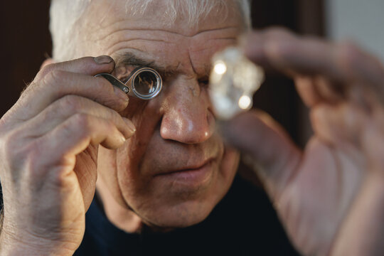 Worker jeweler examining natural rough diamond for grading with magnifying glass and white glove on studio background