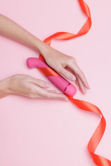 Naklejka premium Pink vibrator on pink background with red ribbon and caucasian female hands