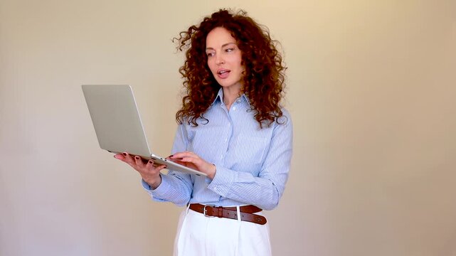Professional business woman with curly hair holding a laptop and giving a presentation against a neutral background