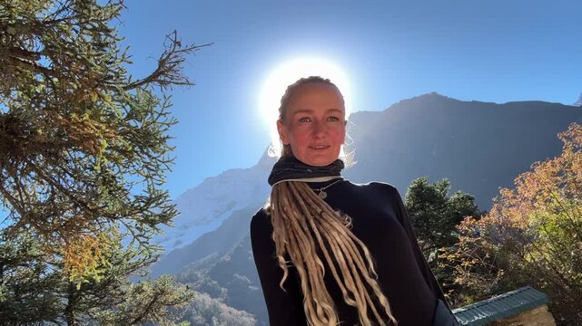 Young woman with dreadlocks smiling in Himalayan mountains on Everest Base Camp trek, Nepal. Backlit sunlight creates halo effect, travel, freedom, happiness, adventure, nature