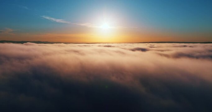 Breathtaking drone shot flying over thick white clouds sunset time. Clear blue sky bright orange sun flare. Summer vacation travel adventure concept. Stunning aerial landscape freedom nature beauty fo