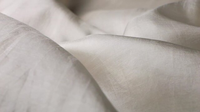 White natural silk fabric develops in the wind. Abstract background of soft waves and flowing texture. Smooth plain material without patterns in light neutral tones. Elegant motion of organic textile.