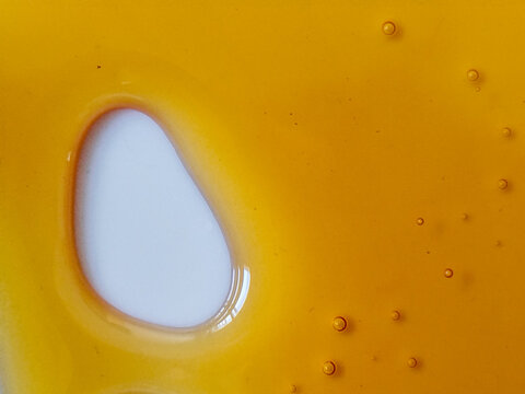 Textura de miel dorada derram&aacute;ndose con peque&ntilde;as burbujas sobre una superficie blanca