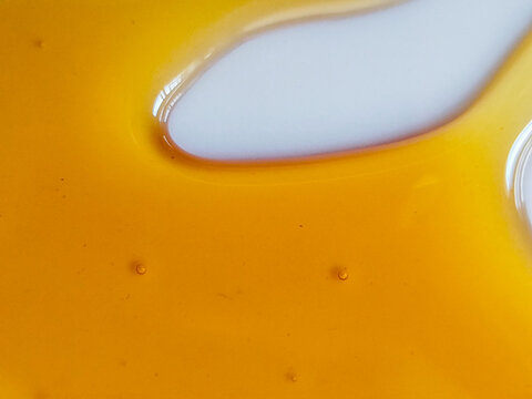 Textura de miel dorada derram&aacute;ndose con peque&ntilde;as burbujas sobre una superficie blanca