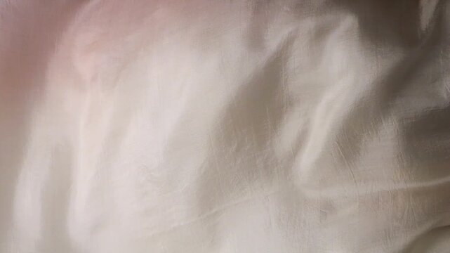 Natural silk fabric waving in the wind. Abstract background of moving soft waves. Beige and white colors of smooth textile. Lightweight natural silk material flowing.