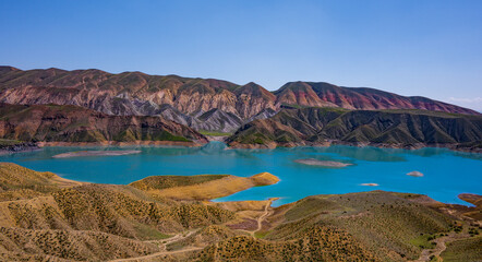 Naklejka premium Turquoise lake surrounded by colorful mountain ridges under bright sky