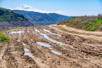 Naklejka premium Muddy trail with water puddles near forested hills