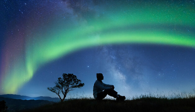 seorang pria duduk dengan latar langit aurora hijau