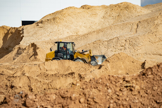 Heavy wheel loader in sandy excavation area with raised soil berms, large aggregate pile, and bucket work for site preparation logistics theme