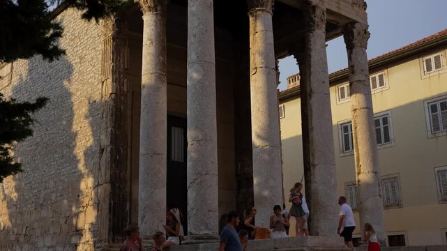 Pula, Croatia - August 17, 2025: Sunlight illuminates the ancient Temple of Augustus in Pula, highlighting its towering Corinthian columns and ornate stone pediment against a clear sky.