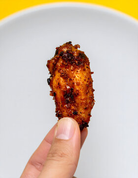 Close Up of Fingers Holding One Crispy Glazed Spicy Chicken Wing on White Background
