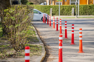 Row of orange red lane separator bollards beside sidewalk edge and bushes on urban street for road safety planning and traffic control use © K