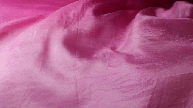 Natural silk fabric flowing in the wind. Soft pink waves creating abstract background. Smooth textile texture with elegant movement. Lightweight material fluttering in slow motion.