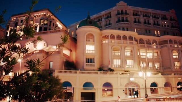 Stunning night time establishing shot of hotel de paris monte carlo in monaco with car and people motion.