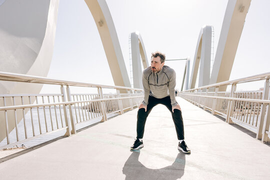 Tired runner resting after jogging workout on modern bridge