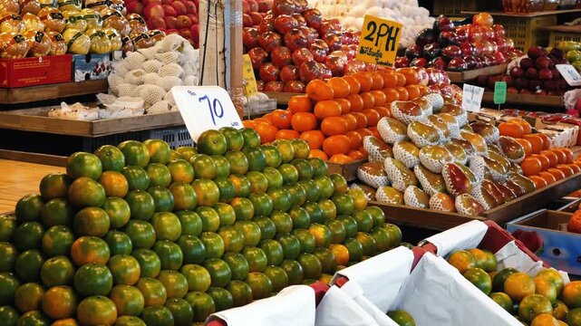 Tangerines stacked in neat rows within outdoor street market, Citrus reticulata and diverse fruits displayed on stalls, organic grocery and local food shopping context, slow motion