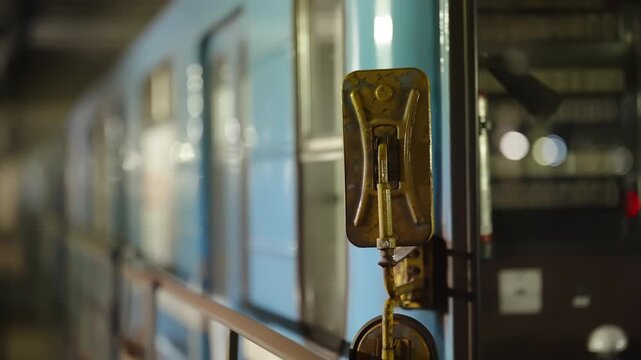 Close-up of a metal handle and latch mechanism on a blue subway train carriage, with the station platform blurred in the background, showcasing transit hardware details
