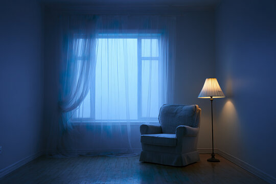 Cozy armchair near glowing floor lamp in dimly lit room with sheer curtains covering large window, creating calm and peaceful evening blue hour ambiance