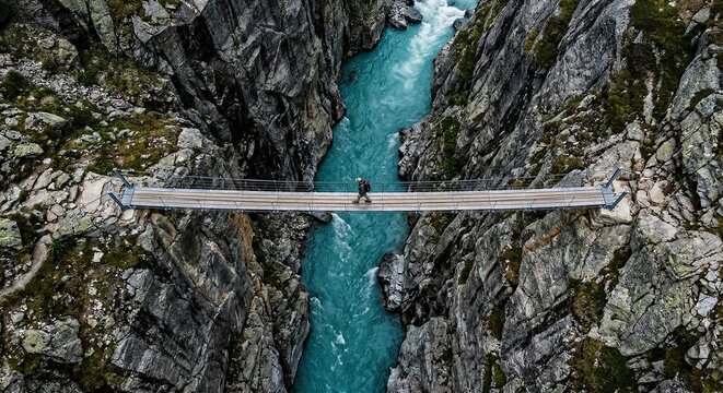 Aerial view of a suspension bridge crossing a narrow turquoise river gorge between dark rocky cliffs.generative AI