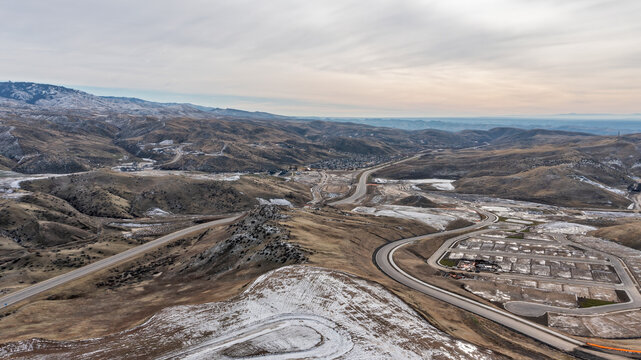 Aerial View of Mountain Highway Corridor Through Snow-Dusted Hills with New Subdivision Development and Overcast Sky