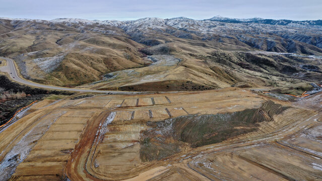 Aerial View of Terraced Hillside Land Grading and Development with Snow-Capped Mountain Range in Background