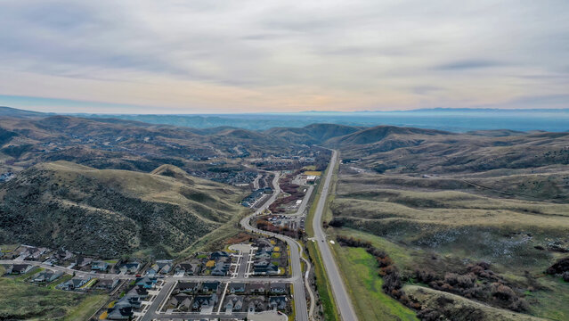 Aerial View of Mountain Highway Through Rolling Hills with Suburban Subdivision Development in Foreground Under Overcast Sky