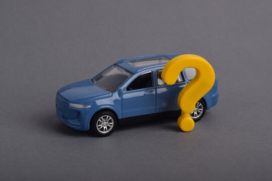Toy car with question mark on grey background. Uncertainty in transportation, buying decision, insurance, and vehicle choice concept.