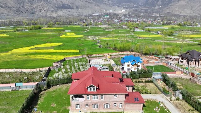 Drone shot flying over colorful residential homes nestled in the vibrant agricultural valleys and mountain ranges of Kashmir.