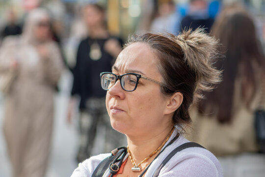 Woman age 45 with glasses stands on a city street and looks aside.