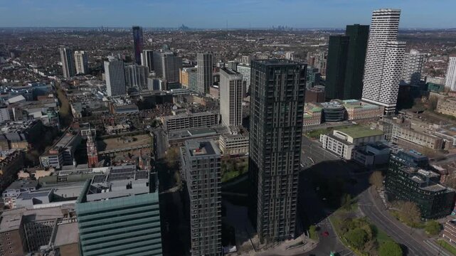 Aerial view of Croydon skyscrapers in city center. Flying above roundabout with light traffic and public transport in motion. Urban area and modern architecture of high rise buildings on a sunny day.