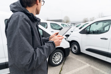 Fleet manager with digital tablet supervising rows of white delivery vans