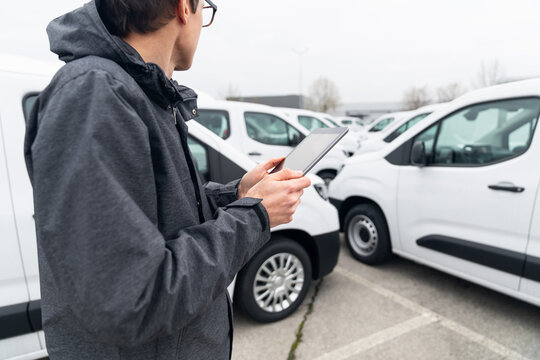 Fleet manager with digital tablet supervising rows of white delivery vans