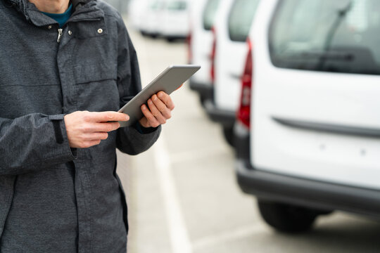 Fleet manager with digital tablet supervising rows of white delivery vans