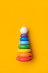Wooden pyramid toy with multicolored rings on bright yellow background top view with space for...
