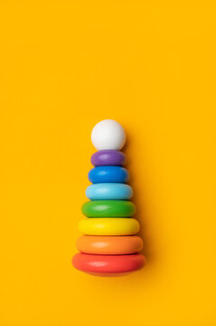 Wooden pyramid toy with multicolored rings on bright yellow background top view with space for text. Montessori children's toy for fine motor skills development. Eco-friendly materials, no plastic 