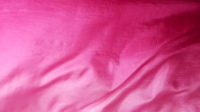 Natural pink silk fabric blowing in the wind. Soft abstract waves of real silk material. Smooth flowing textile with blurry floral pattern. Elegant motion of vibrant pink fabric.