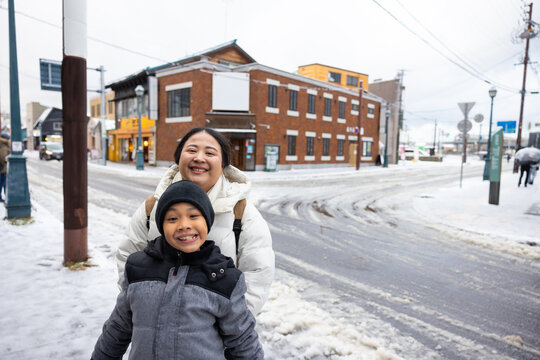 Family travel and Vacation together, Asian mother and son Traveler on Sidewalk with Cityscape Background. street. Boy Enjoying Sunny Winter Day in Picturesque Town. child posture suggests curiosity
