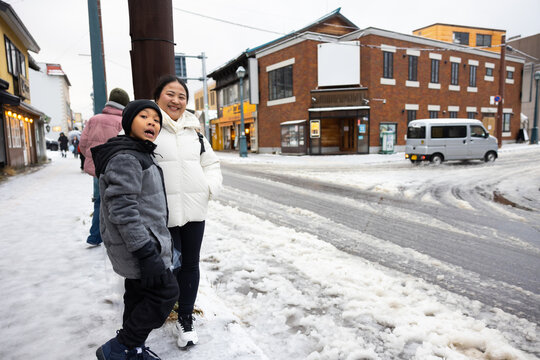 Family travel and Vacation together, Asian mother and son Traveler on Sidewalk with Cityscape Background. street. Boy Enjoying Sunny Winter Day in Picturesque Town. child posture suggests curiosity