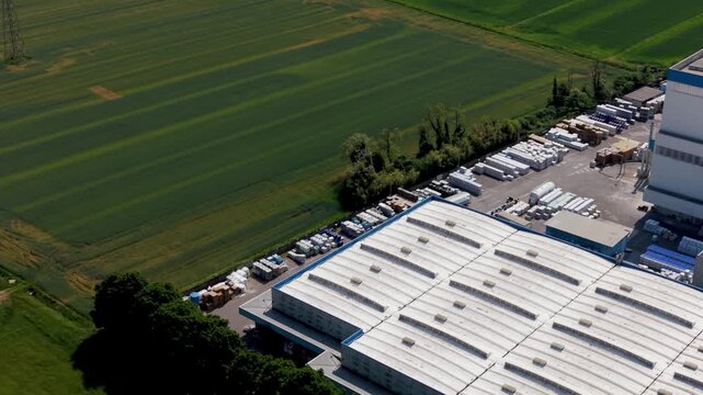 Industrial Landscape: Aerial view showcases a commercial property featuring a warehouse, vehicles and a farm field, presenting the convergence of industry and agriculture.